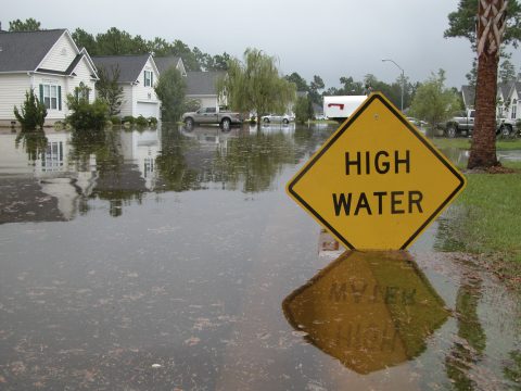 Neighborhood flooded. Sign warns of high water.